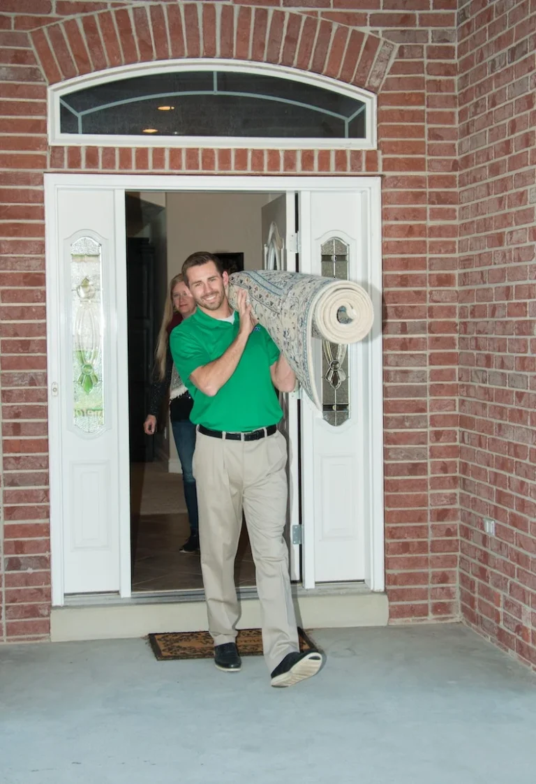 Chem-Dry technician carrying a rolled area rug out of a home
